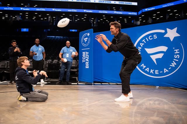 <p>Fanatics</p> Tom Brady tosses a football with Boston at an event hosted by Fanatics and Make-A-Wish