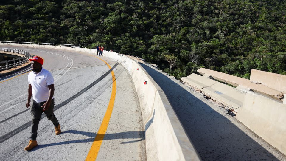 A man walks past the damaged part of the bridge, where the bus crashed through barriers. - Siphiwe Sibeko/Reuters