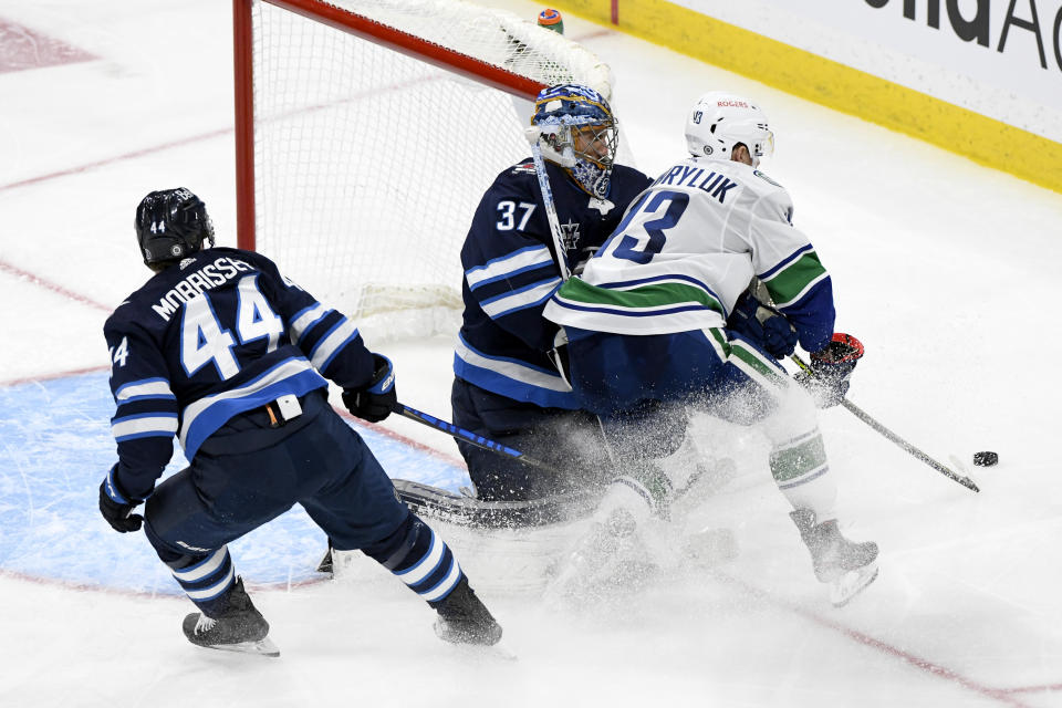 Vancouver Canucks' Jayce Hawryluk (13) collides with Winnipeg Jets goaltender Connor Hellebuyck (37) during the third period of an NHL hockey game Tuesday, May 11, 2021, in Winnipeg, Manitoba. (Fred Greenslade/The Canadian Press via AP)