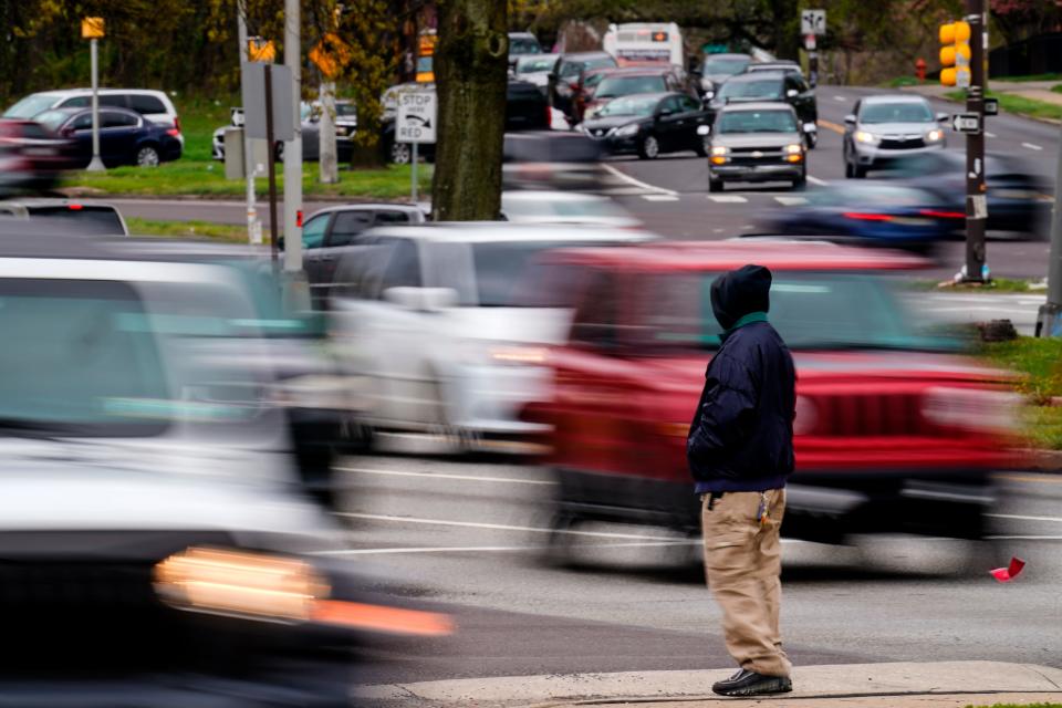 A pedestrian waits to cross Roosevelt Boulevard, in Philadelphia, Tuesday, April 19, 2022. Roosevelt Boulevard is an almost 14-mile maze of chaotic traffic patterns that passes through some of the city's most diverse neighborhoods and Census tracts with the highest poverty rates. Driving can be dangerous with cars traversing between inner and outer lanes, but biking or walking on the boulevard can be even worse with some pedestrian crossings longer than a football field and taking four light cycles to cross.