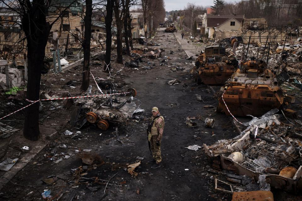 A Ukrainian serviceman in uniform stands on a road lined with destroyed Russian tanks and other debris