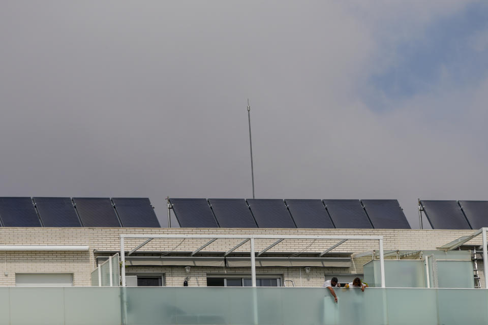 A couple stand in their balcony, with solar panels are on the roof of the building in Rivas Vaciamadrid, Spain, Thursday, Sept. 15, 2022. The energy crisis is accelerating the installation of solar panels by residential communities in Spain who want to become self-sufficient. Recent legislation has allowed so-called "energy communities" to generate renewable power through collective installations. (AP Photo/Manu Fernandez)