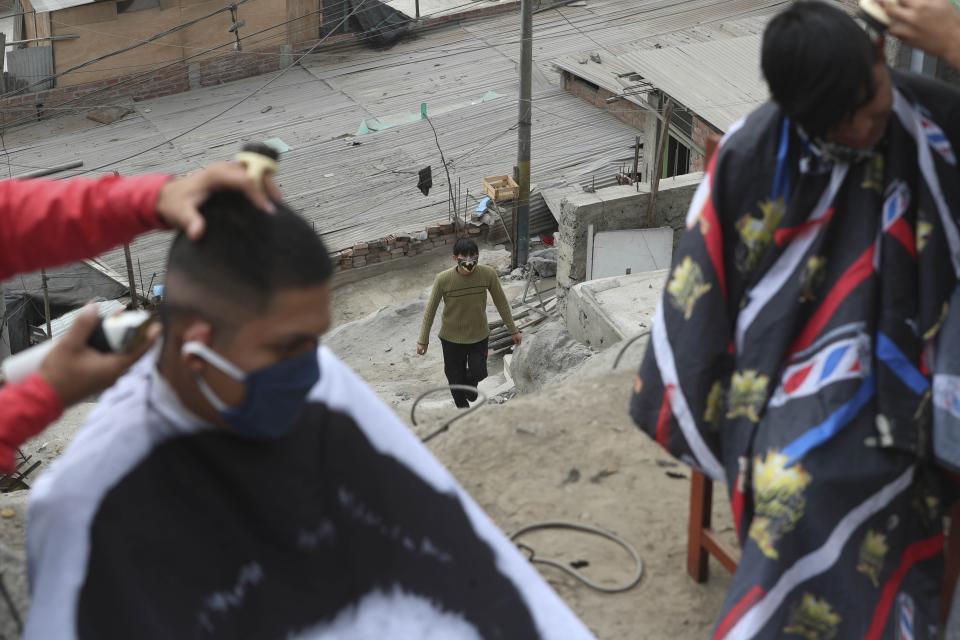 A resident watches as his neighbors receive free haircuts from Josue Yacahuanca, 21-year-old barber, and his brother Luis, in the San Juan de Lurigancho neighborhood of Lima, Peru, Friday, June 19, 2020. Like thousands of businesses across Peru, Yacahuanca's barbershop _ called D Barrio Shop _ closed its doors March 16 under quarantine orders. Since then, he's watched his personal finances be pulverizing. But, he's brushed it off, deciding to help others with the skills he has. (AP Photo/Martin Mejia)