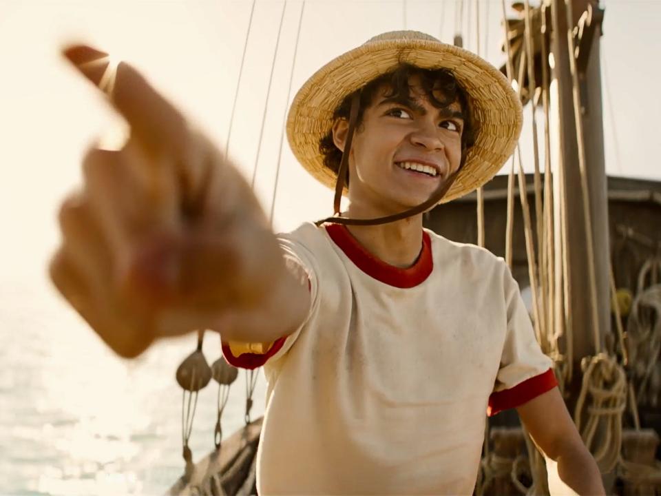 iñaki godoy as luffy in one piece, sitting on a boat and pointing forward with a smile on his face