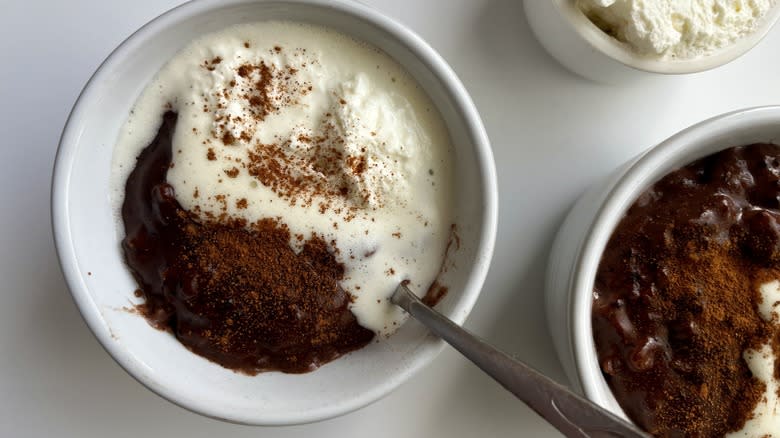 a bowl of chocolate rice pudding topped with whipped cream and cinnamon with a spoon in it