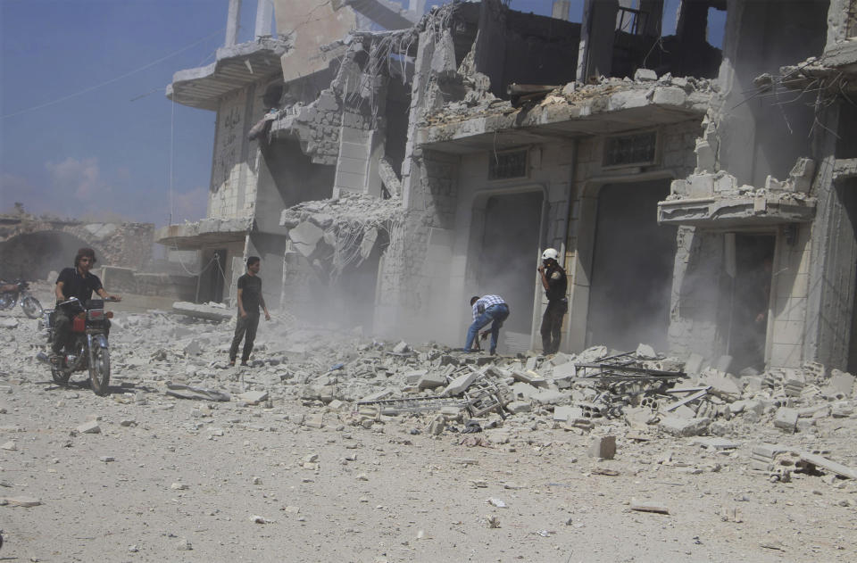 This photo provided by the Syrian Civil Defense group known as the White Helmets, shows civilians and civil defense worker, right, next to a destroyed building that was attacked by a Syrian government airstrike, in Hobeit village, near Idlib, Syria, Sunday, Sept. 9, 2018. The White Helmets and a conflict monitoring group said Sunday that government and Russian forces have resumed their bombing of the opposition's last stretch of territory in the country, killing an infant girl and damaging a hospital. (Syrian Civil Defense White Helmets via AP)