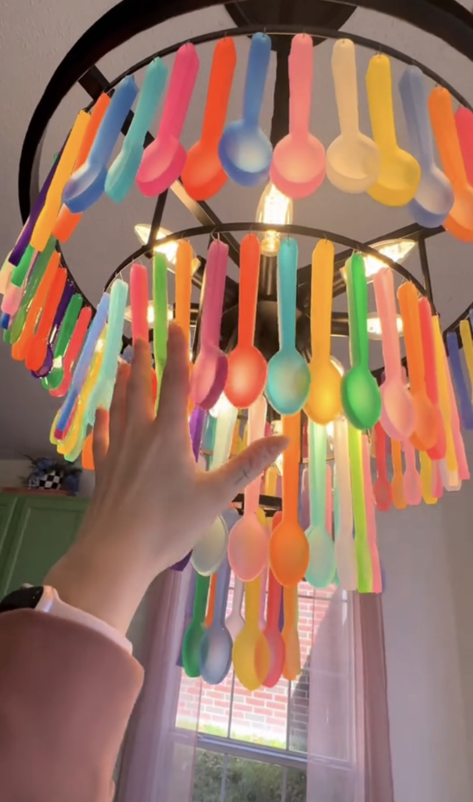 Hand touching a colorful chandelier made with dangling utensils in a room