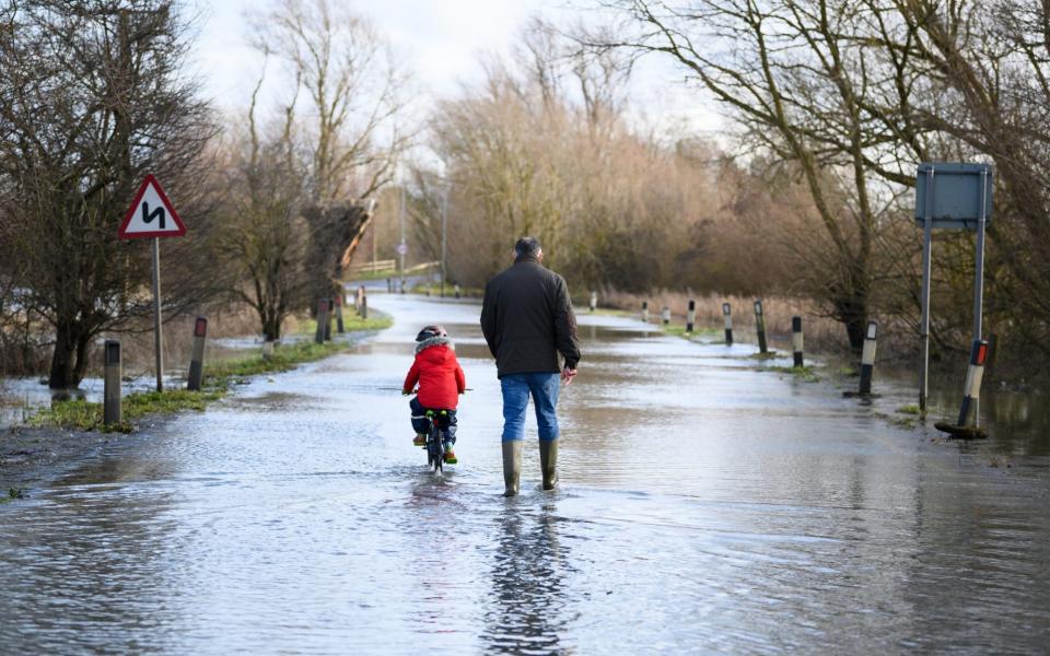 A child cycles along the flooded road by the side of the River Great Ouse after it was closed  - Getty