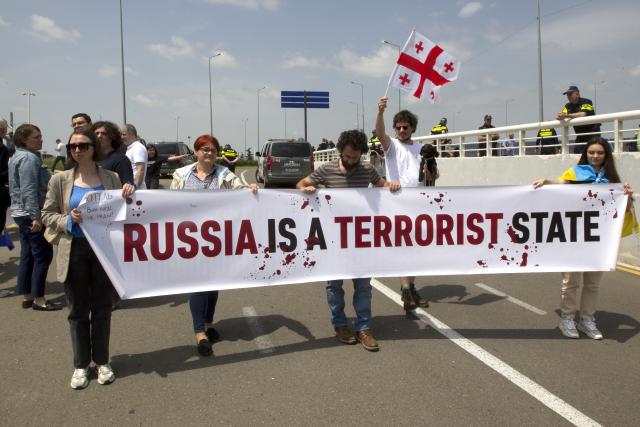 Georgian opposition activists with a Georgian national flag and a banner, protest against the resumption of air links with Russia at the International Airport outside Tbilisi, Georgia, Friday, May 19, 2023. Direct flights resumed on Friday between Russia and Georgia amid protests and sharp criticism from the South Caucasus nation's president, just over a week after the Kremlin unexpectedly lifted a four-year-old ban despite rocky relations. (AP Photo/Shakh Aivazov)