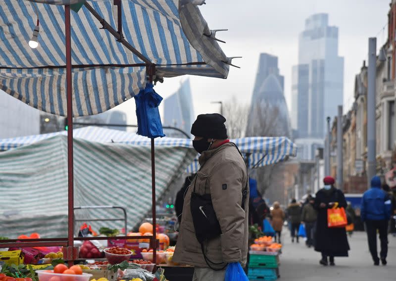 People shop at market stalls, with skyscrapers of the CIty of London financial district seen behind, in London