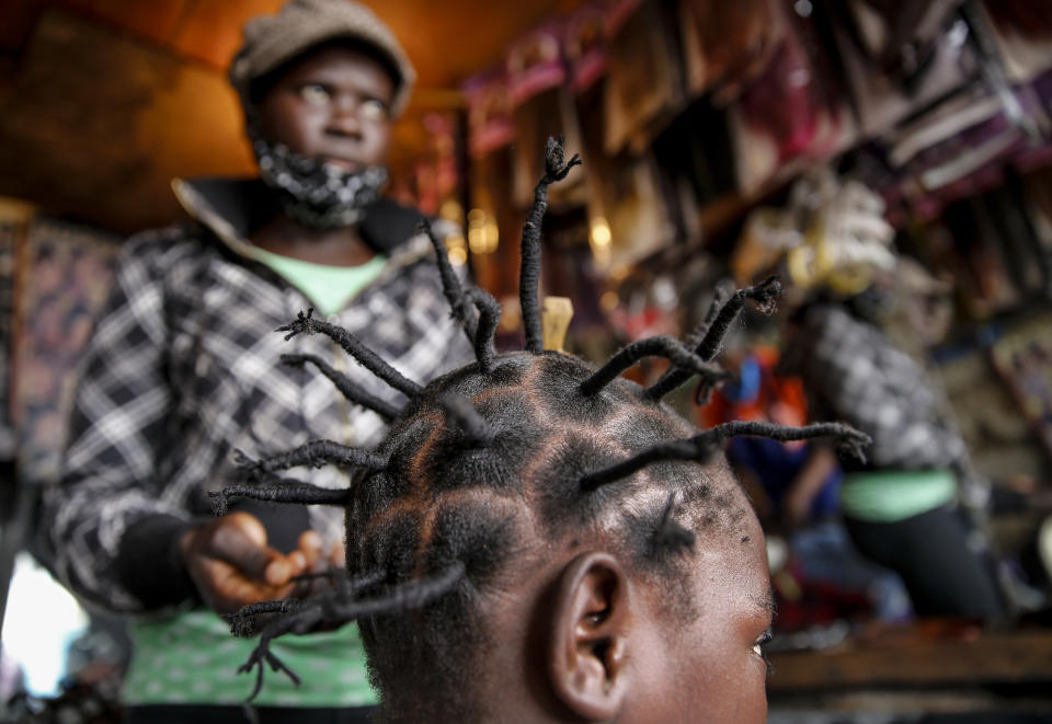 FILE - In this Sunday, May 3, 2020 file photo, Gettrueth Ambio, 12, has her hair styled in the shape of the new coronavirus, at the Mama Brayo Beauty Salon in the Kibera slum, or informal settlement, of Nairobi, Kenya. The coronavirus has revived a hairstyle in East Africa, one with braided spikes that echo the virus' distinctive shape, with the growing popularity in part due to economic hardships linked to virus restrictions. (AP Photo/Brian Inganga, File)
