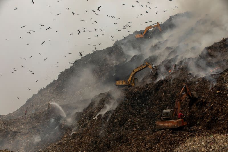 Firefighters and excavators try to douse fire as smoke billows from burning garbage at the Ghazipur landfill site in New Delhi