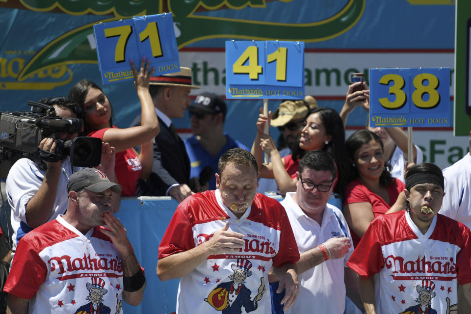 Geoffrey Esper, left, Joey Chestnut, center, and Matt Stone finish the men's competition of Nathan's Famous July Fourth hot dog eating contest, Thursday, July 4, 2019, in New York's Coney Island. (AP Photo/Sarah Stier)