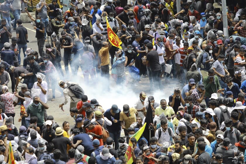 Protesters react as a tear gas shell fired by police lands next to them in Colombo, Sri Lanka, Saturday, July 9, 2022. Sri Lankan protesters demanding that President Gotabaya Rajapaksa resign forced their way into his official residence on Saturday, a local television report said, as thousands of people took to the streets in the capital decrying the island nation's worst economic crisis in recent memory. (AP Photo/Amitha Thennakoon)