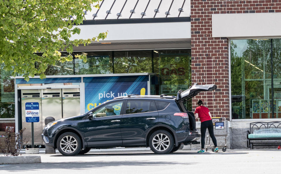 Person loading groceries into car at a curbside pickup area outside a store