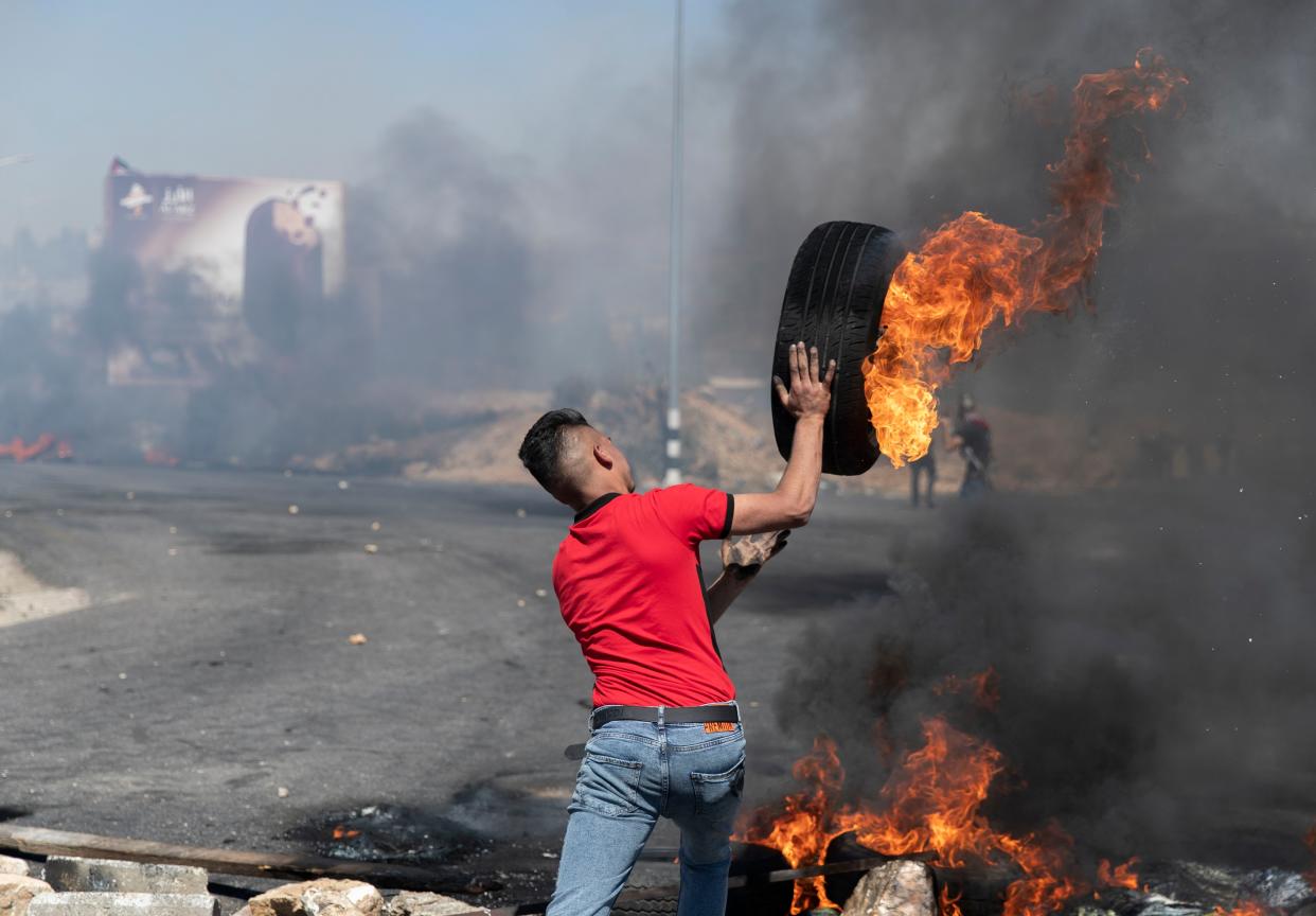 A Palestinian protester rolls a burning tire toward Israeli army soldiers during clashes at the northern entrance of the West Bank city of Ramallah on Friday, May 14, 2021. Palestinian health officials said that several Palestinians were killed by Israeli army fire during protests that took place in several locations across the West Bank on Friday.