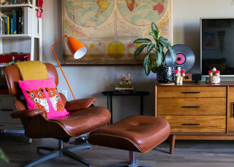 A eames style lounge chair with brown leather and pink decorative pillow.