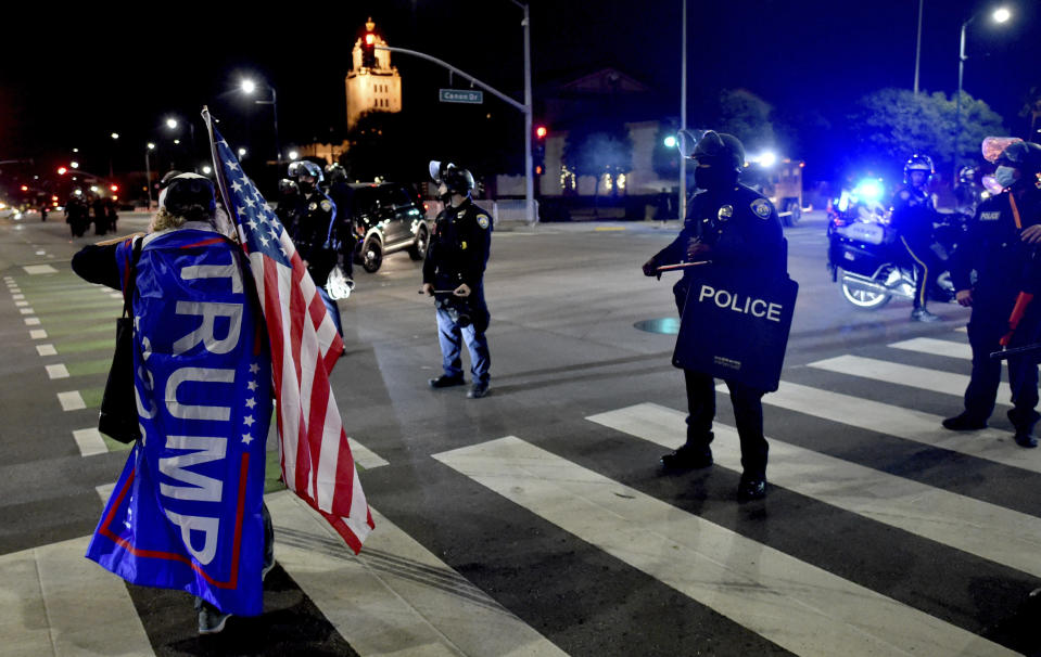 A protester carrying a flag in support of President Donald Trump and an American flag yells toward Beverly Hills Police as the authorities declare the protest an unlawful assembly and attempt to clear out the demonstrators during a pro-Trump rally in front of Beverly Gardens Park on the corner of Santa Monica Boulevard and Canon Drive in Beverly Hills, Calif., on Wednesday, Jan. 6, 2021. (Keith Birmingham/The Orange County Register via AP)