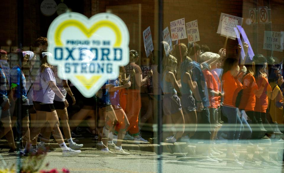 Reflected in some of the Oxford Strong signs in business windows in downtown Oxford, marchers carry signs and chant as they march in the March For Our Lives Oxford event on Saturday, June 11, 2022. Students, teachers and parents shared their stories of loss following the shooting at the school and demanded that lawmakers enact gun control laws to keep these tragedies from happening again. When the crowd reached the high school, it held a moment of silence to honor and remember the teens who were gunned down, Madisyn Baldwin, Tate Myre, Justin Shilling, and Hana St. Juliana.