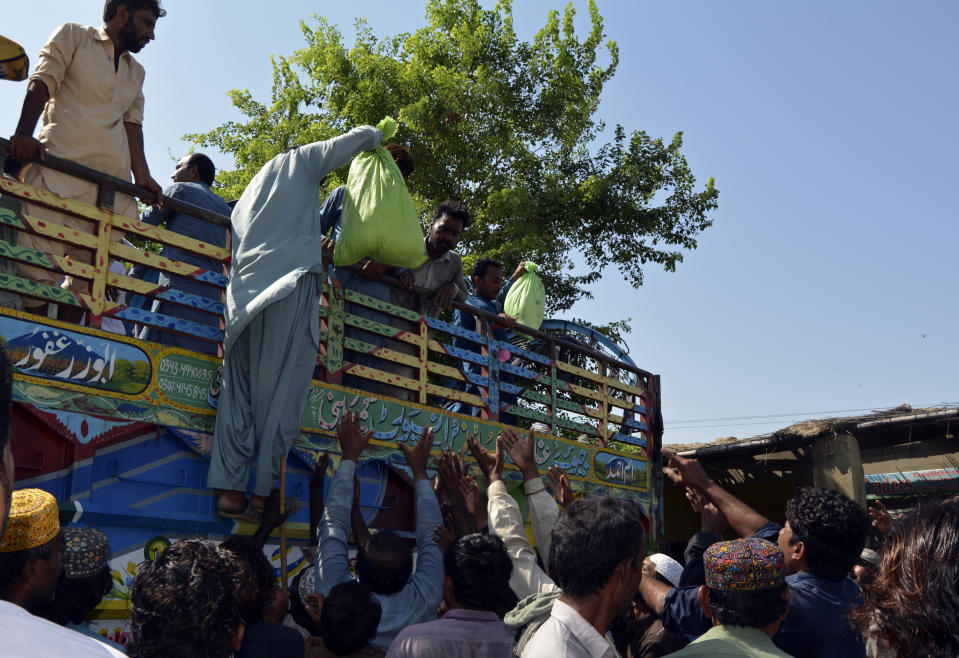 Displaced families line up to receive food aid as they take refuge in an open area, after fleeing their flood-hit homes, in Multan, Pakistan, Wednesday, Aug. 31, 2022. Officials in Pakistan raised concerns Wednesday over the spread of waterborne diseases among thousands of flood victims as flood waters from powerful monsoon rains began to recede in many parts of the country. (AP Photo/Shazia Bhatti)