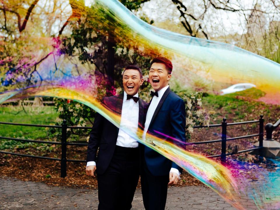 A couple smiles as two iridescent bubbles surround them in a park.