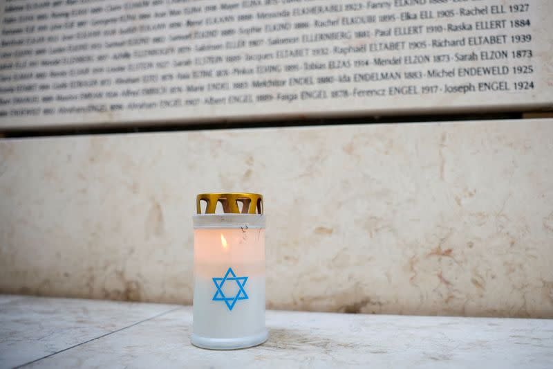 A candle is seen in front of the Wall of Names at the Shoah Memorial in Paris