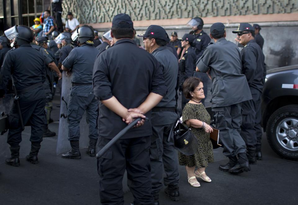 <p>A woman walks amid riot policemen during a protest organized by artisanal and small-scale gold miners in Lima, Peru, March 24, 2014. The miners marched in the country’s capital for the fifth day, asking the government to repeal regulations aimed at formalizing informal miners. (Photo: Rodrigo Abd/AP) </p>