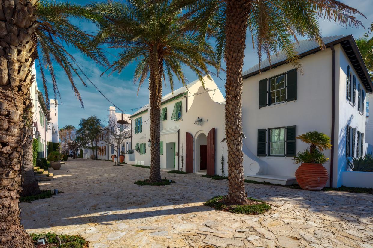 A beach house with a trademark white stone facade in Alys Beach surrounded by palm trees and blue skies