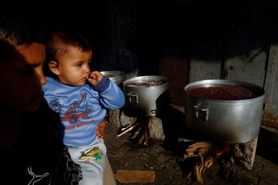 2023年10月15日，加薩南部甘尤尼斯一名男童抱著年紀更小的孩子，望著正在烹煮的食物。路透社