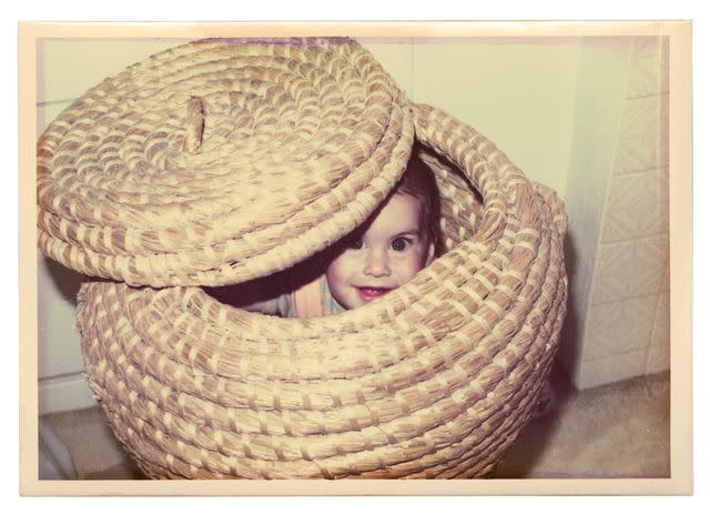 <p>Courtesy of HarperCollins</p> A mischievous Amy, hiding in a basket in an old family photo. The singer, who was born in Sept. 1983, would have turned 40 this year.