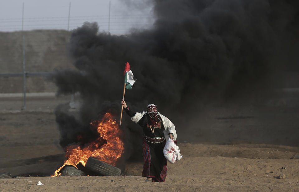 FILE - In this Oct. 5, 2018 file photo, a Palestinian woman wearing a traditional thobe, carries a Palestinian flag during a protest at the Gaza Strip's border with Israel. The thobe, a brightly embroidered robe for women, has long been a staple of Palestinian life, sewn by village women and worn at weddings and parties. Now it’s gaining prominence as a softer symbol of Palestinian nationalism, competing with the classic keffiyeh. Rashida Tlaib proudly wore her thobe to her historic swearing-in as the first Palestinian American member of Congress, inspiring women around the world to tweet photos of themselves in their ancestral robes. (AP Photo/Khalil Hamra, File)