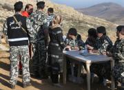 Lebanese General Security forces check the identity card of a Lebanese woman, center, as she leaves the Tfail village, in the Ras al-Haref mountains at the Lebanese-Syrian border, eastern Lebanon, Tuesday April 22, 2014. A Lebanese convoy of soldiers, clerics and Red Cross officials delivered aid Tuesday to a remote village near the Syrian border that was bombed by Syrian government aircraft and blocked by Lebanese militants fighting alongside President Bashar Assad’s forces in the civil war next door. Hezbollah fighters have been patrolling the area on the Lebanese side and fighting has flared up inside Syria, cutting Tfail’s residents off from all sides for months. (AP Photo/Hussein Malla)