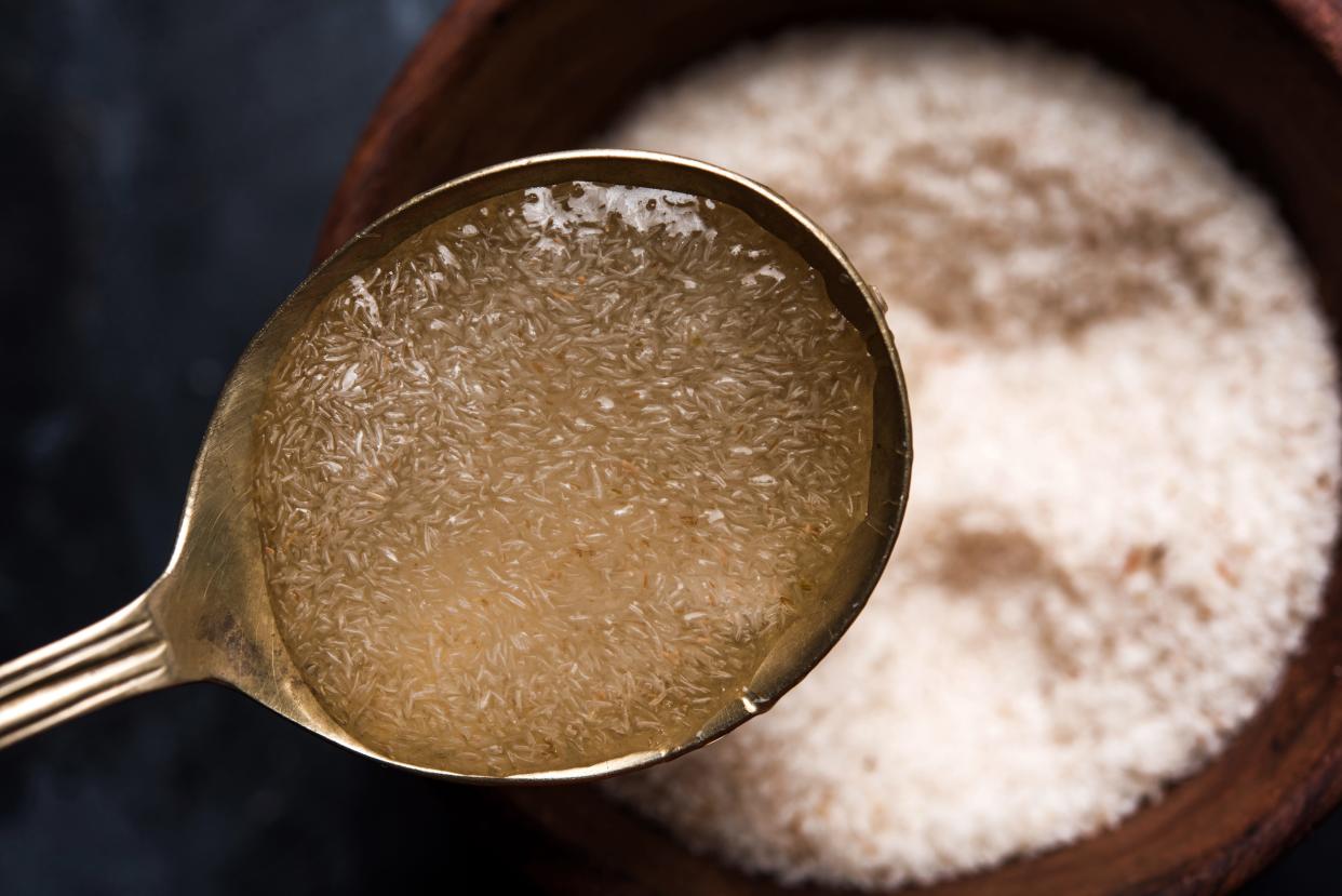 Up-close image of a spoon holding gelatinous psyllium husk. Out-of-focus in the background is a wooden bowl holding dry psyllium husk.