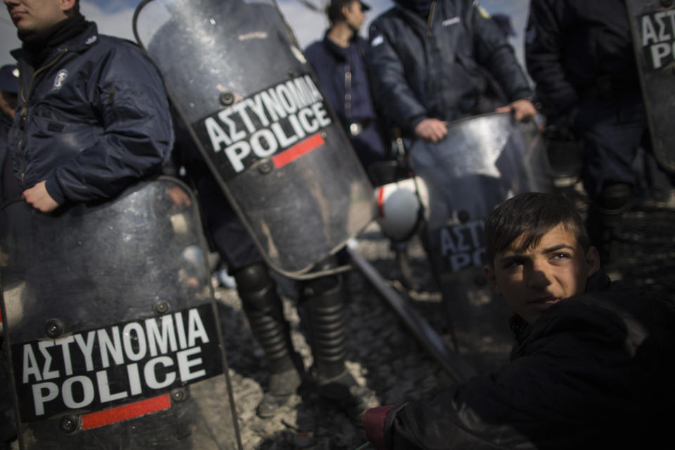 A young boy sits in front of police officers as a train attempts to pass in Idomeni.&nbsp;