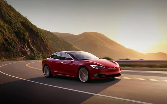 Red Model S driving on curving road with mountains in the background