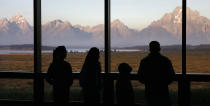 FILE - In this Aug. 28, 2016 file photo visitors watch the morning sun illuminate the Grand Tetons from within the Great Room at the Jackson Lake Lodge in Grand Teton National Park north of Jackson, Wyo. On Tuesday, March 24, 2020, the National Park Service announced that Yellowstone and Grand Teton National Parks would be closed until further notice, and no visitor access will be permitted to either park. (AP Photo/Brennan Linsley,File)