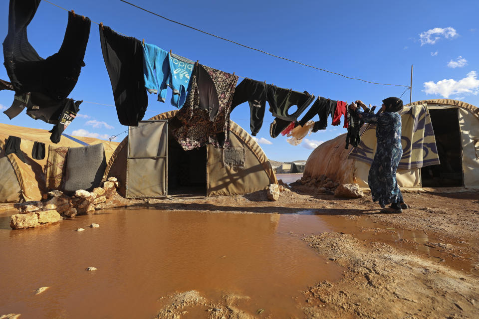 FILE - A woman hangs laundry in a flooded refugee camp in Idlib province, Syria, Dec. 21, 2021. Syrians in the last major rebel stronghold in the war-ton country are living in fear of the effects of Russia closing down the only border crossing into the northwestern province of Idlib. Aid agencies warn that if Russia vetoes the resolution that would maintain two border crossing points from Turkey to deliver humanitarian aid, food would be depleted in Idlib and surrounding areas by September, 2022, putting the lives of some 4.1 million people, at risk. (AP Photo/Ghaith Alsayed, File)