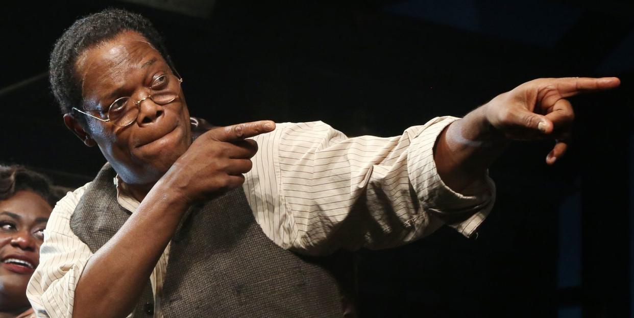 samuel l jackson, wearing a white shirt, gray vest and glasses, points off camera with both hands