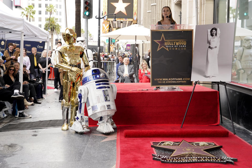 Billie Lourd habla durante una ceremonia en honor a su madre, la fallecida actriz Carrie Fisher, que aparece en una fotografía a la derecha, al develar una estrella póstuma en el Paseo de la Fama de Hollywood junto a los personajes de "Star Wars" C-3PO y R2-D2 en Los Ángeles el jueves 4 de mayo de 2023. La fecha se conoce también como Día de Star Wars, en homenaje a las películas de "Star Wars" en las que Fisher interpretó a la Princesa Leia. STAR WARS-CARRIE FISHER