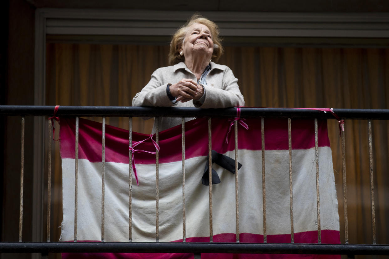 A woman stands in her balcony with a banner representing the Spanish flag and a black ribbon in memory of the victims of COVID-19 in Madrid, Spain, Tuesday, May 12, 2020. Roughly half of 47 million Spaniards are stepping into a softer version of the country's coronavirus strict confinement and are beginning to socialize, shop in small establishments and enjoy a meal or a coffee in restaurants and bars with outdoor seating Tuesday. (AP Photo/Manu Fernandez)