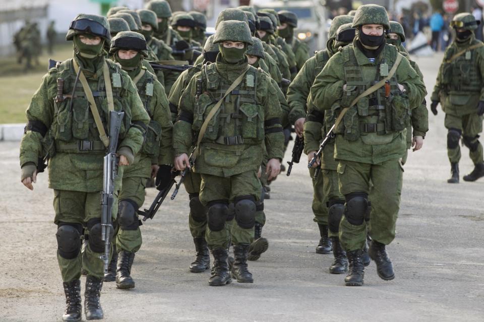 Military personnel, believed to be Russian servicemen, walk outside the territory of a Ukrainian military unit in the village of Perevalnoye outside Simferopol