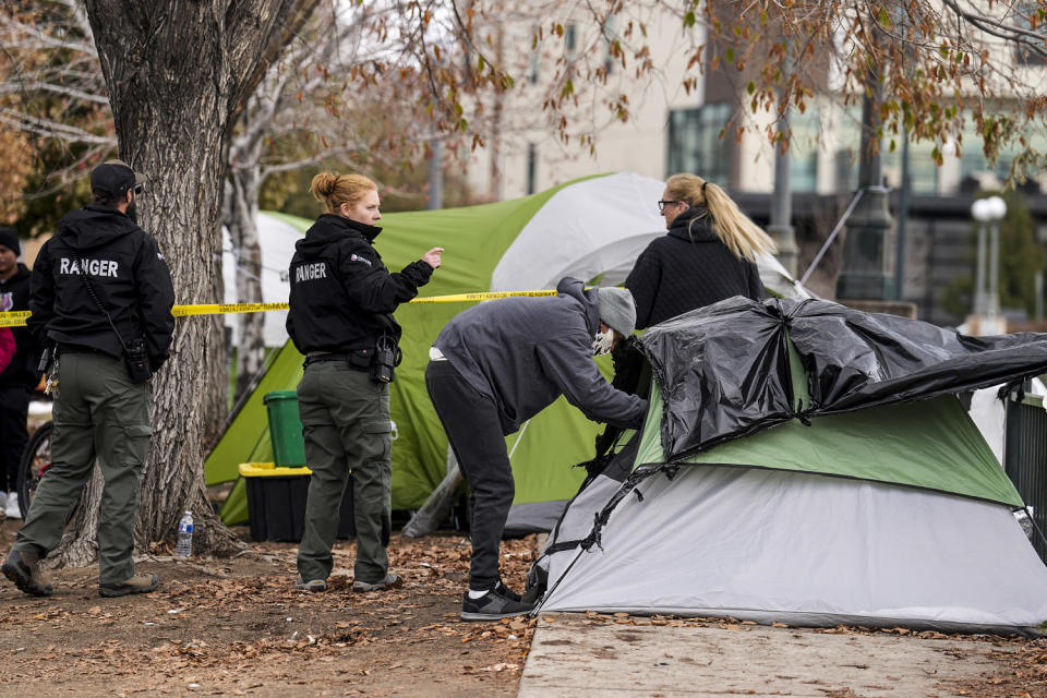 A person collects items from a tent as Denver Parks Department rangers string police tape during a city-sponsored sweep of an encampment (David Zalubowski / AP file)