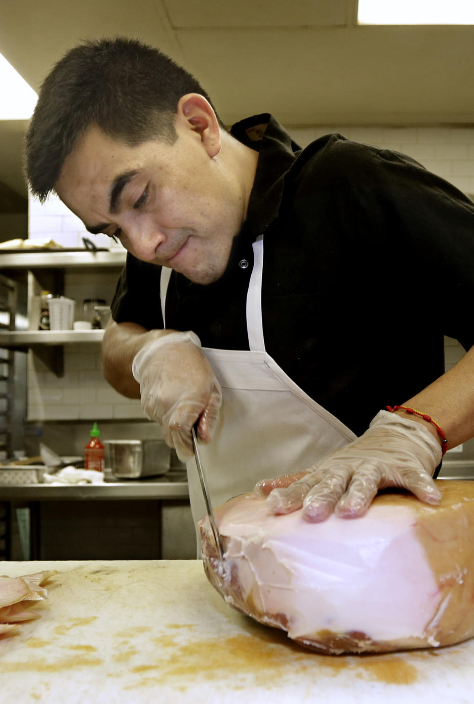 In this photo taken Wednesday, March 12, 2014, Luis Escamilla wears gloves as he trims a ham at the Hock Farm Restaurant in Sacramento, Calif. at the Hock Farm restaurant in Sacramento, Calif. Under a bill signed last year by Gov. Jerry Brown, chefs and bartenders in California must keep bare hands off food going straight to the plate or the drink glass, and must use gloves or kitchen utensils such as tongs. California, where the law took effect Jan. 1 and will begin enforcement starting in July, will join 41 other states banning bare-hand contact with ready-to-eat food. In February,after receiving a petition from bartenders calling for an exemption for the "disposable glove law" the law's author, Assemblyman Richard Pan, D-Sacramento, a pediatrician, has introduced a bill to repeal the new regulation and revisit the entire issue.(AP Photo/Rich Pedroncelli)