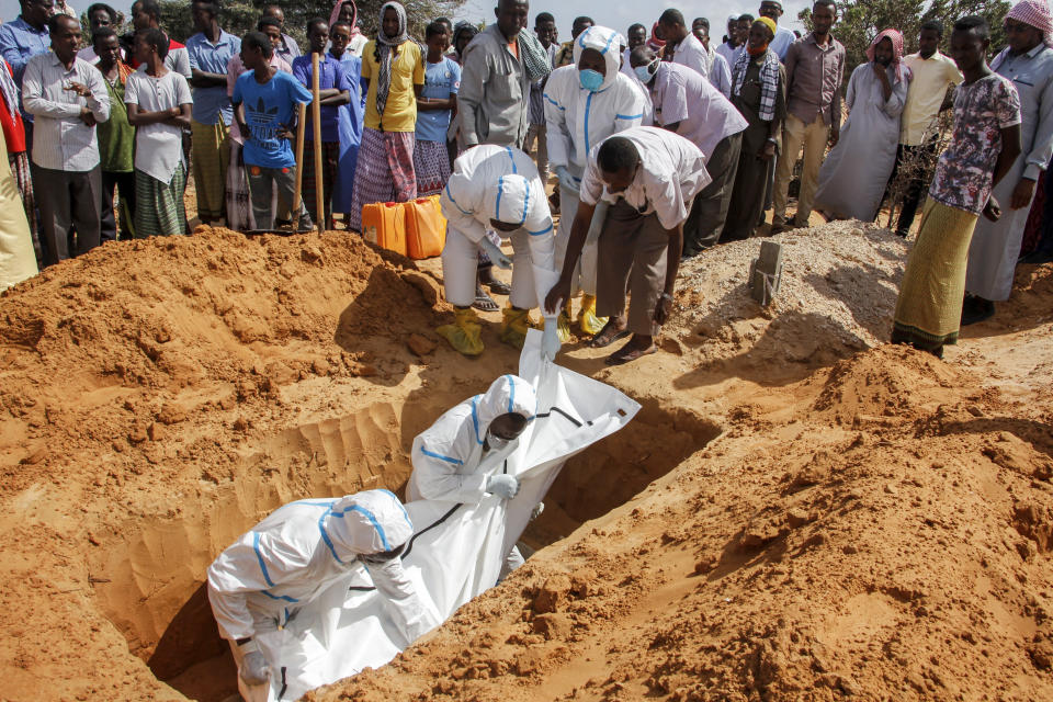 In this photo taken Wednesday, May, 13, 2020, medical workers wearing protective suits, surrounded by mourners, bury the body of Ibrahim Hassan, 56, at a cemetery in Mogadishu, Somalia. His brother says he died of the coronavirus. Years of conflict, instability and poverty have left Somalia ill-equipped to handle a health crisis like the coronavirus pandemic. The uncertainty has led to fear, confusion and panic even after authorities have tried to keep the public informed about the outbreak. (AP Photo/Farah Abdi Warsameh)