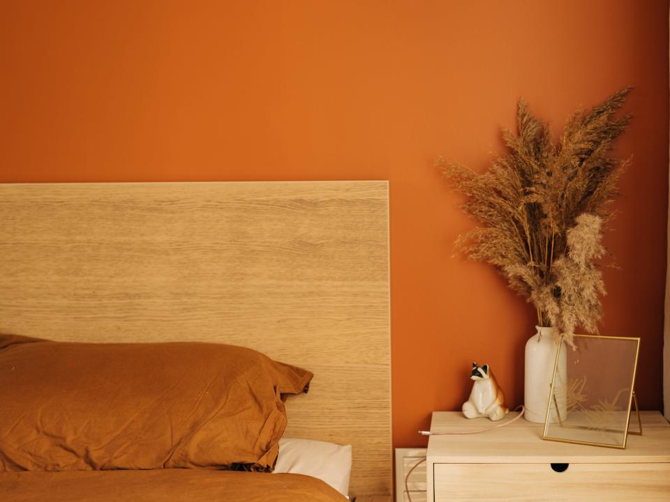 A bed with a wooden headboard and a wooden side table in front of a terracotta wall