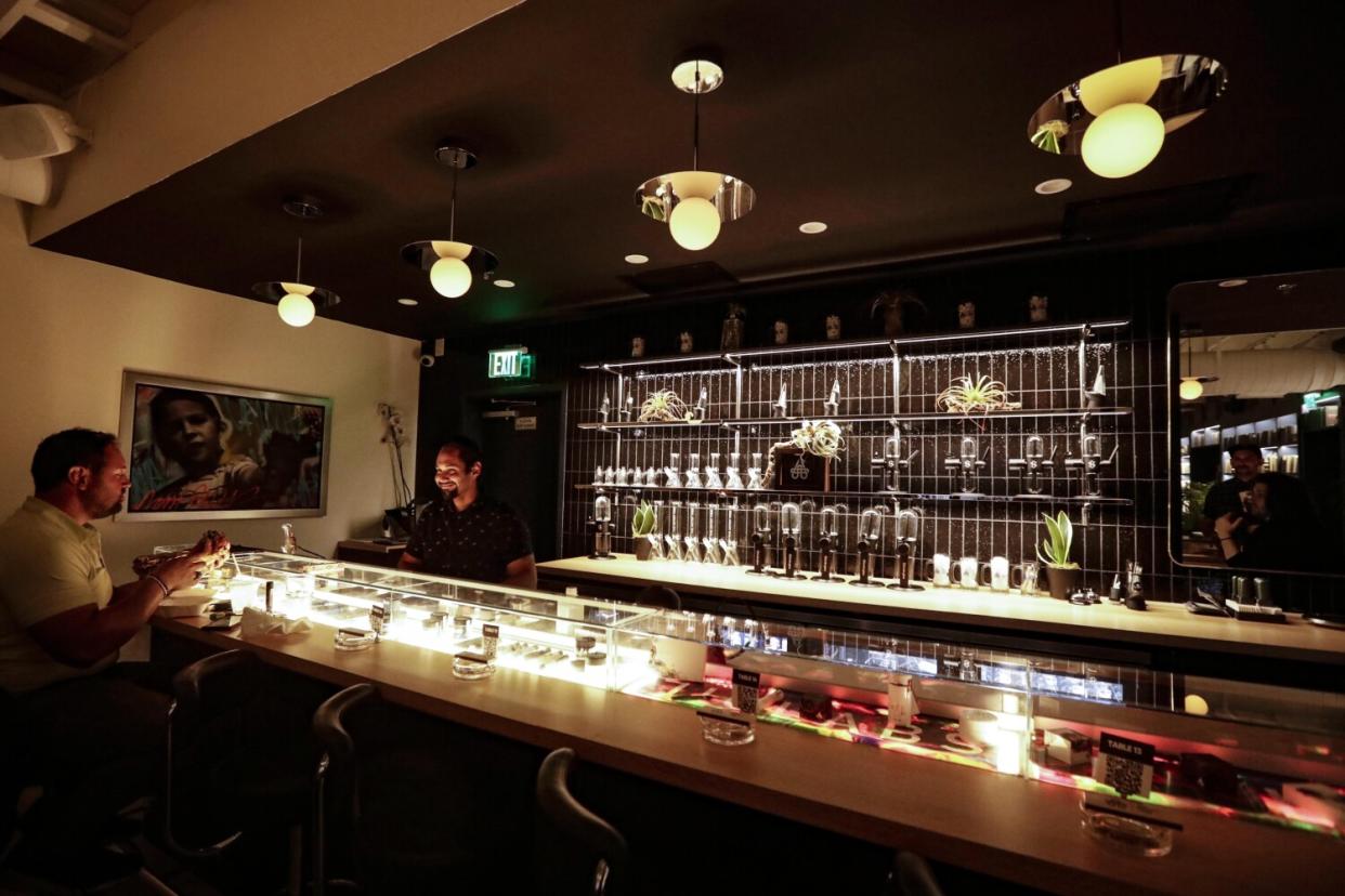 A man standing behind a dispensary bar talking to a customer