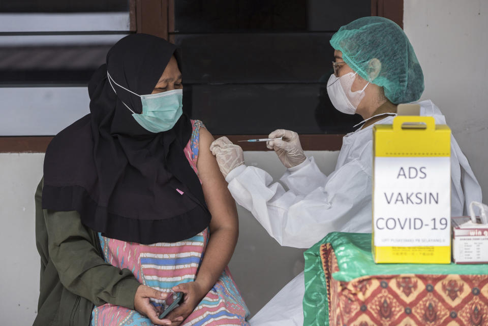 Nurse Novita Sirait, right, gives a shot of the COVID-19 vaccine to a colleague at a community health center in Medan, North Sumatra, Indonesia, Tuesday, Jan. 26, 2021. The world's fourth most populous country has started giving COVID-19 vaccine to health workers this month as its first stage of a plan to vaccinate two-thirds of its population of about 270 million people. (AP Photo/Binsar Bakkara)