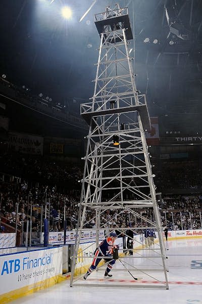 A man in hockey gear skates underneath a metal scaffold meant to look like oil machinery.