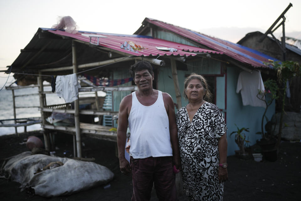 Residents Joseph Vargas, president of a fishing association, left, and his wife Wilma Abanil stand outside their house near a liquefied natural gas power plant in Santa Clara, Batangas province, Philippines on Tuesday, Aug. 8, 2023. The Philippines is seeing one of the world's biggest buildouts of natural gas infrastructure. Vargas says most communities have seen no benefit from the power plants built so far. (AP Photo/Aaron Favila)