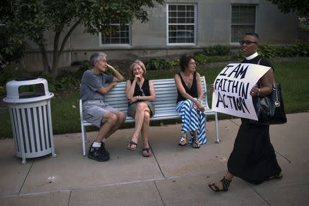 A woman holding a placard walks past bystanders sitting on a bench as she takes part in a march by clergymen to the County Prosecutor Bob McCulloch's office to protest the shooting death of unarmed black teen Michael Brown, in Clayton, Missouri August 20, 2014. REUTERS/Adrees Latif